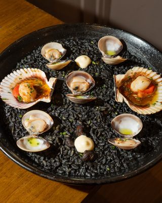 Black rice paella with scallops, clams and aioli served in the pan