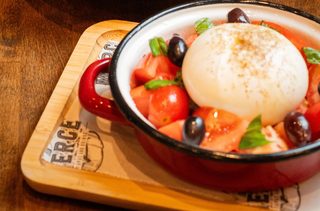 Burrata in a small pan with tomatoes, olives and basil